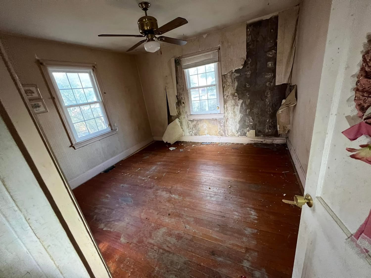 Room before renovation with worn wood flooring and damaged wall covering